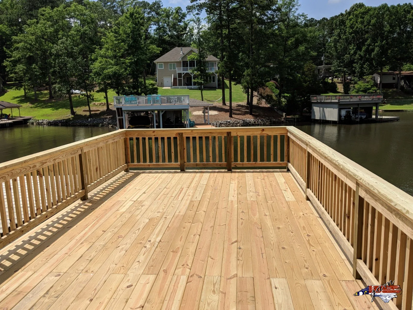New wood deck with railings overlooking a lake and boathouse
