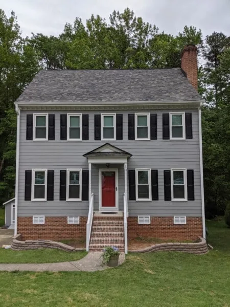 Two-story colonial with gray siding, black shutters, and a red front door