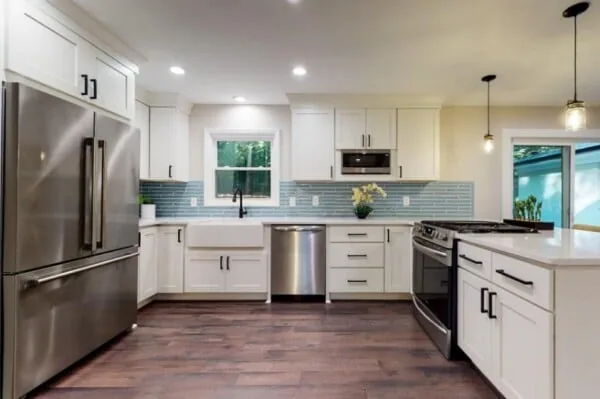 Renovated kitchen with white cabinets, stainless appliances, and a blue tile backsplash